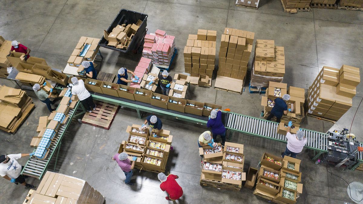 Overhead view of workers packing food products into boxes along a conveyor line in a large food distribution facility