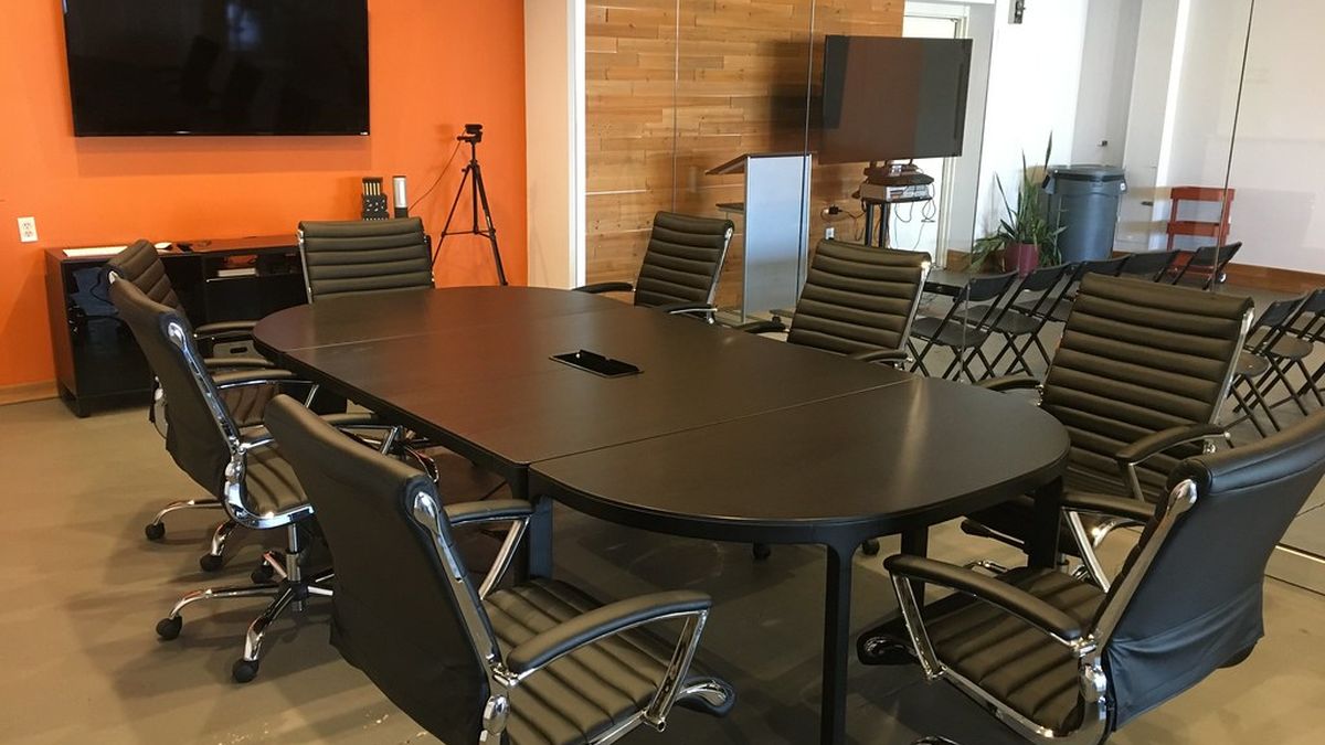Empty meeting room in a coworking hub with a long dark table, black office chairs and wall-mounted screens