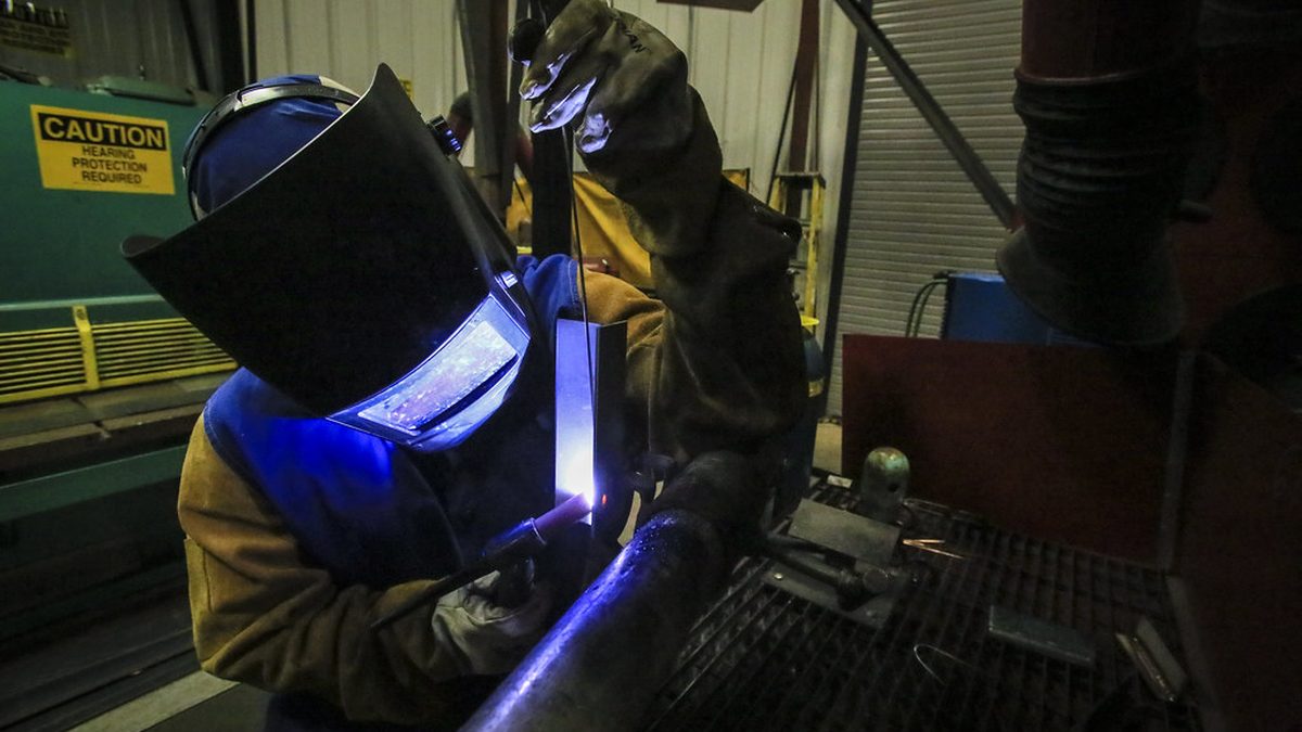 Welder in protective gear fabricating a steel tube in an industrial metal shop